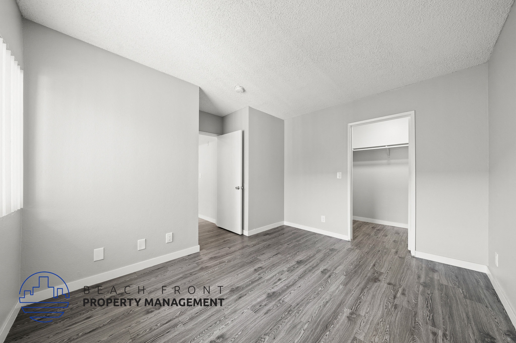 A room with wooden flooring and white walls, with a logo for Beach Front Property Management in the bottom left corner.